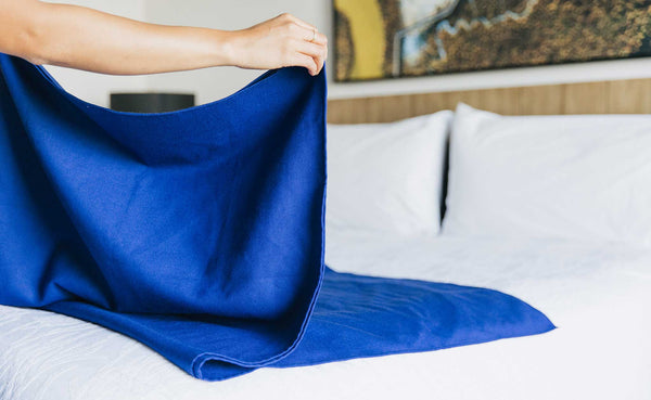 A Large Shepherd's Wool Utility Cloth in Neela Blue being folded on a hotel bed.